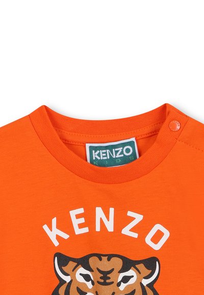 T-shirt en coton orange à col rond, avec un graphisme de tigre et le texte "KENZO" en blanc. Détail de bouton-pression à l'épaule.