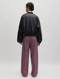 Zwarte leren bomberjack met een gathered zoom, gedragen over losse roze broeken. Effen textuur, minimalistisch ontwerp en hoge kraagdetails.