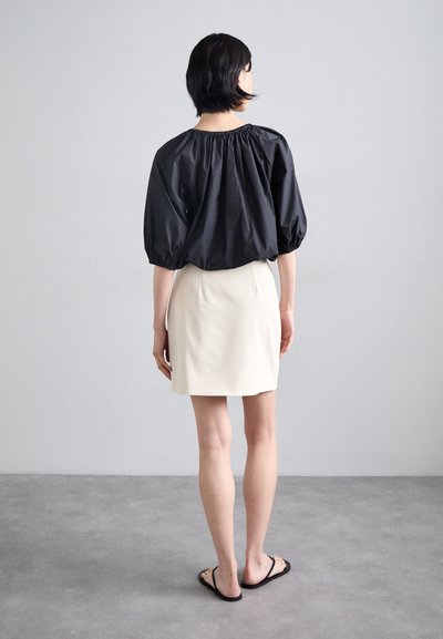 Black puff-sleeve top with gathered neckline, paired with a fitted beige mini skirt and black flip-flops. Minimalist design, smooth textures.
