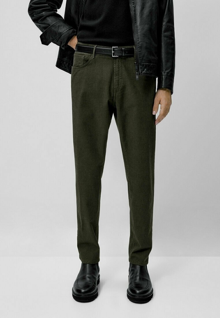 Tummanvihreät puuvilla-chinonhousut, kapealahkeiset, sivutaskuilla ja vyöllä. Yhdistetty mustaan nahkatakkiin ja kiiltäviin mustiin nyörisaappaisiin.