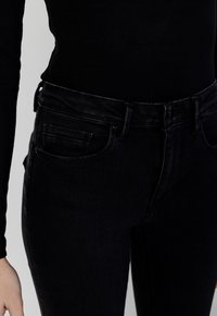 Jeans in denim nero con un design aderente, caratterizzati da una cintura tradizionale, tasche frontali e una superficie liscia.