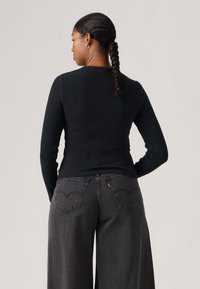 Top negro de manga larga con textura acanalada, combinado con jeans de tiro alto y corte holgado en gris oscuro, que presentan bolsillos traseros prominentes y detalles de costura.