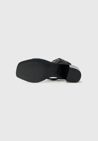 Svart sandal med en glatt læroverdel og en tykk hæl. Har en spenne-rem og en teksturert gummi såle for godt grep.