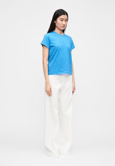 Mėlyni medvilniniai marškinėliai su apvalia kaklo linija ir trumpomis rankovėmis, derinami su aukštakulniais platėjantys balti kelnės. Paprastas dizainas, be raštų.