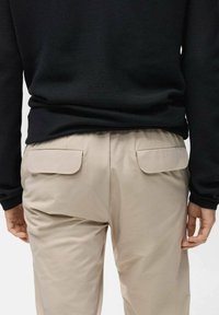 Black textured long-sleeve top paired with light beige trousers featuring two back patch pockets with flap closures.