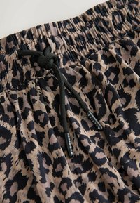 Taille élastique avec cordon noir sur un short ou un pantalon en tissu beige et noir à imprimé léopard.