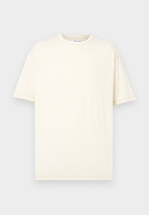 Schlichtes, elfenbeinfarbenes Kurzarm-T-Shirt mit Rundhalsausschnitt und sichtbaren Nahtstichen an Schultern und Ärmeln vor hellgrauem Hintergrund.