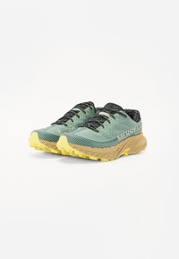 Trail running shoes in light green textured upper, black laces, and yellow rubber sole with aggressive tread patterns for traction.