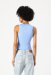 Top corto senza maniche in cotone a coste azzurro chiaro con scollatura rotonda e dettaglio del logo sul retro, abbinato a jeans in denim chiaro.