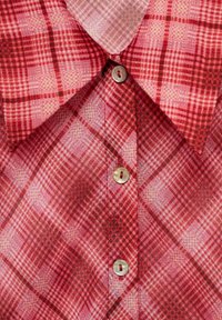 Col de chemise à carreaux rouges et roses avec trois boutons blancs alignés verticalement sur la patte de boutonnage avant.