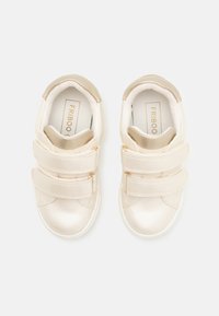 Baskets crème avec deux sangles Velcro, tige synthétique lisse, bout arrondi, semelle intérieure rembourrée et accents dorés minimalistes.