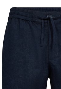 Marineblaue Leinenhose mit elastischem Bund, Kordelzugverschluss und einer seitlichen Tasche. Glatte Textur mit dezenten Webdetails.