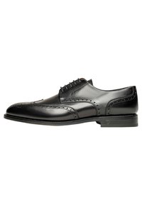Chaussure habillée en cuir noir avec un design à bout fleuri et des perforations, lacets plats et un petit talon. Texture lisse avec une finition brillante.