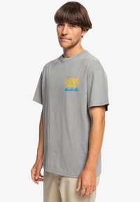 Light gray cotton t-shirt with a relaxed fit. Features a multicolored graphic of waves and sun on the left chest. Short sleeves and crew neck.