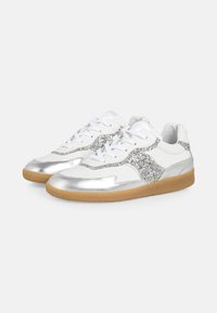 White sneakers with silver accents and glitter detail. Features a smooth texture, rounded toe, and a gum sole. Classic lace-up design.