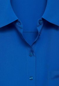 Chemise bleu vif à col avec des boutons sur le devant et une poche poitrine visible sur le côté droit.