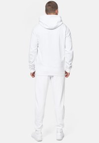 White hoodie and matching joggers, both made of soft fabric. The hoodie features a spacious hood and ribbed cuffs, with a relaxed fit.