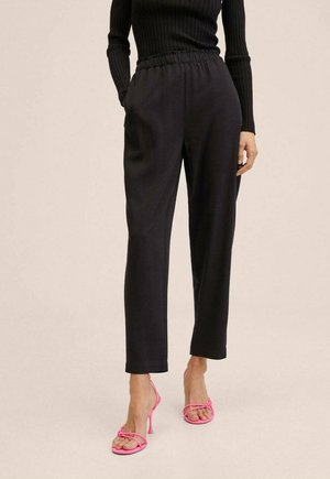 Vrouw draagt zwarte broek met hoge taille en elastische tailleband, gecombineerd met een zwarte geribde longsleeve top en felroze hakken met bandjes.