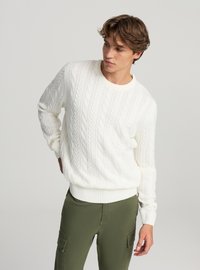 Biały sweter dziany z wzorem warkocza, z okrągłym dekoltem, ściągaczami na mankietach i dole. Połączony z oliwkowymi spodniami typu cargo o luźnym kroju.
