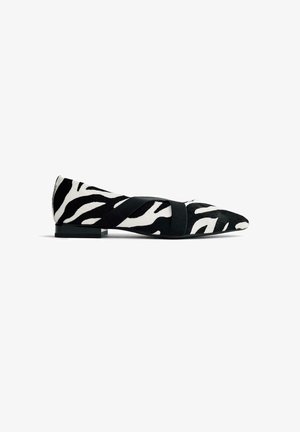 Zapato plano con estampado de cebra, material de pelo negro y blanco, punta afilada y una tira elástica negra en el medio del pie. Tacón bajo.