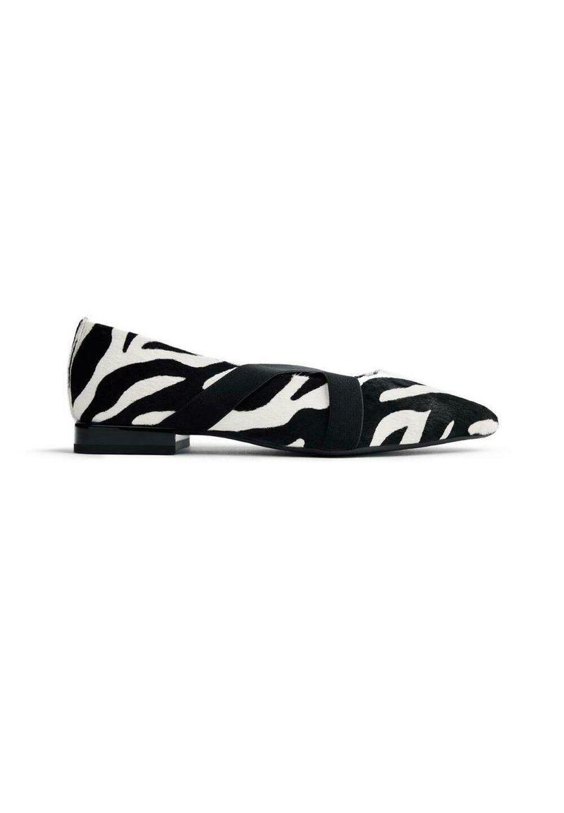 Zapato plano con estampado de cebra, material de pelo negro y blanco, punta afilada y una tira elástica negra en el medio del pie. Tacón bajo.