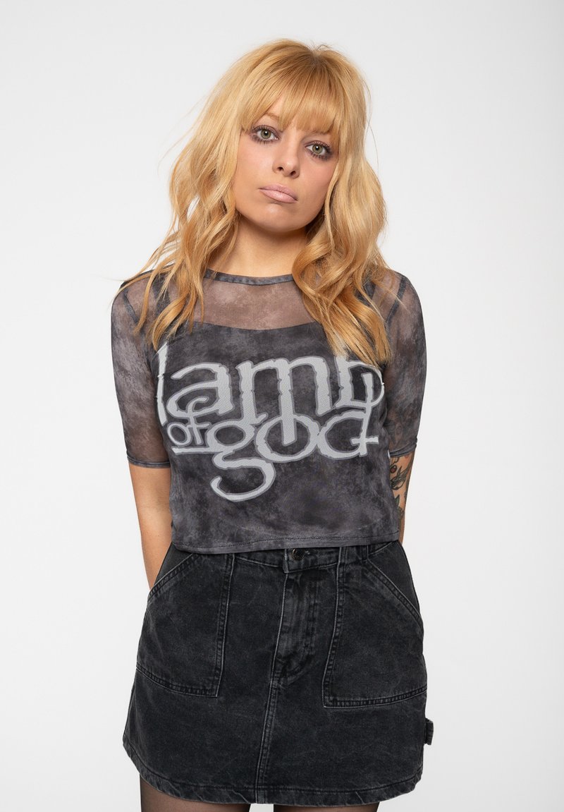 Black graphic tee with "Lamb of God" in gray letters, featuring a sheer overlay and short sleeves, paired with a black denim skirt.