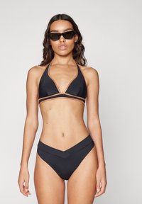 Black bikini with a halter top featuring tan accents, V-shaped design, and a matching high-waisted bottom. Smooth texture, minimal coverage.