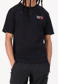 Czarny T-shirt z krótkim rękawem wykonany z bawełny, z nadrukowanym białym i czerwonym logo na górnej lewej stronie. Prosty dekolt typu crew, luźny krój.