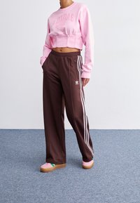 Rosa kort sweatshirt med "ADIDAS"-text, bruna vida byxor med vita sidostipes och rosa sneakers med gröna accenter.