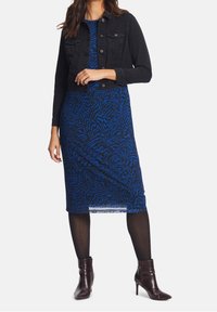 Svart denimjacka över en blå klänning med swirlmönster; modellen har svarta strumpbyxor och bordeauxfärgade ankelstövlar.