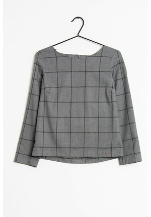Grijze blouse met lange mouwen met zwart ruitenpatroon, boothals en klein metalen logo-label onderaan, hangend aan een zwarte kledinghanger.