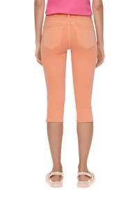 Pfirsichfarbene, taillierte Jeans mit einem cropped Schnitt, fünf Taschen und einem leicht ausgefransten Saum. Getragen mit hellen Sandalen.