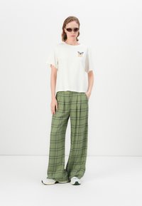 White short-sleeve t-shirt with butterfly graphic, paired with green plaid wide-leg pants. Model wears tinted sunglasses and sneakers.