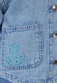 Helles blaues Denim-Jacke mit einer linken Tasche, die blaue Blumenstickerei zeigt, und silbernen Druckknöpfen auf der Vorderseite.