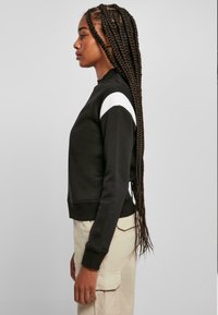 Czarna bluza z okrągłym dekoltem, z białymi akcentami na ramionach. Miękka faktura i dopasowany krój, zestawiona z jasnymi spodniami cargo.