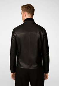 Zwarte leren jas met een slank model, staande kraag en een gladde textuur. Heeft minimale stiksels en een schone, moderne uitstraling.