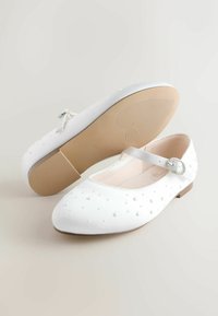 Weiße Ballerinas mit einem weichen Stoff-Obermaterial, verziert mit kleinen erhabenen Punkten, einem Riemen mit dekorativer Schnalle und einer flachen Gummisohle.
