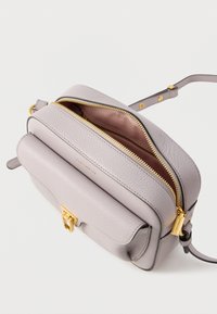 Gray leather crossbody bag with a gold zip closure and clasp. Features a textured finish and a single adjustable strap. Interior highlights a pink lining.