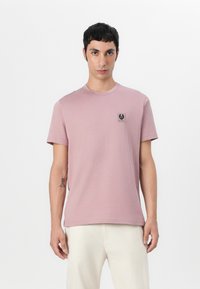 Tricou din bumbac roz, cu mâneci scurte, guler rotund și un mic patch cu logo negru pe pieptul stâng. Textură netedă și croială clasică.