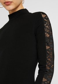 Black top with a mock neck, featuring long sleeves made of intricate black lace. Smooth texture with a fitted silhouette.