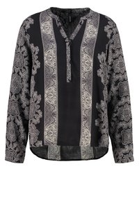 Blouse noire à manches longues avec des motifs paisley blancs complexes et un col à mi-pli. Tissu doux avec un ourlet arrondi.