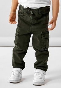 Pantaloni cargo verdi con polsini elasticizzati, molteplici tasche e vita regolabile con cordino. Abbinati a sneakers bianche.