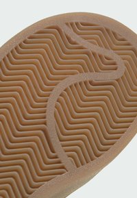 Gros plan d'une semelle de chaussure en caoutchouc marron avec motifs texturés en zigzag et rainures courbes pour l'adhérence.