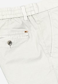 Hellgraue Hose mit elastischem Bund, ausgestattet mit einer Seitentasche, gestickten Details und einem kleinen orangefarbenen Etikett in der Nähe der Tasche.