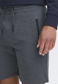 Graue Baumwollmischungshorts mit elastischem Bund, Kordelzug und seitlicher Zipper-Tasche. Glatte Textur und lässige Passform.