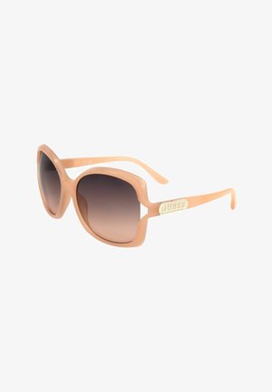 Occhiali da sole quadrati oversize beige con lenti marroni sfumate e placca dorata con logo "GUESS" sulle astine.
