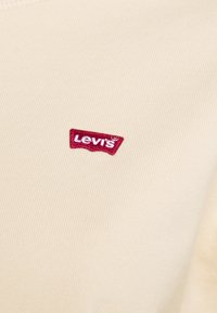Béžová tkanina s malou červenou nášivkou loga Levi's vyšitým bílou nití na povrchu.