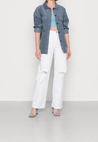 Giacca in velluto blu, top corto azzurro, jeans bianchi a gamba larga e strappati, e sandali con tacco blu. Concentrati sulla trama e sul contrasto cromatico.