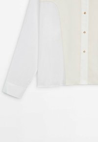Chemise blanche à manches longues avec un panneau avant crème texturé, trois boutons dorés et une patte de boutonnage blanche.