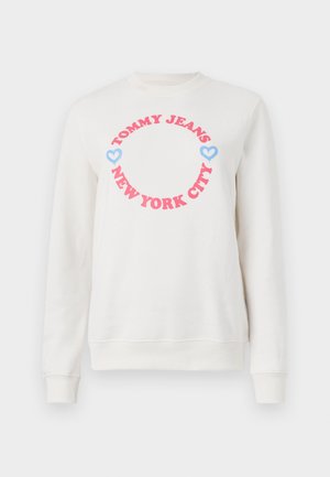 Balta džemperis ar apaļu grafiku, kurā redzams "TOMMY JEANS" rozā krāsā un "NEW YORK CITY" zemāk, papildināts ar zilām sirdīm. Mīksta kokvilnas auduma.